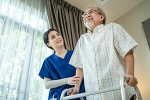 A professional caregiver providing home health care in Phoenix helps an older man walk safely around the house.