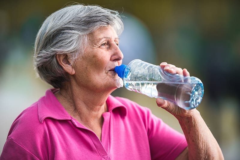 An older woman drinks water, one way to help prevent heat stroke in seniors.